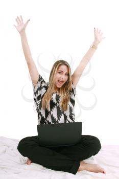 Woman sitting on the bed with a laptop computer and arms up - isolated 