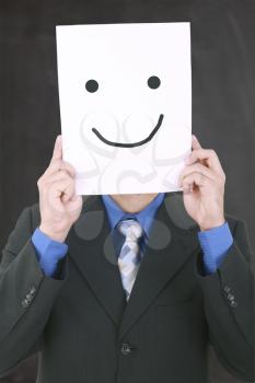 Young businessman hiding his face with a white billboard with a smiley face on it 
