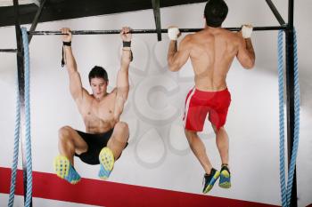 athletic group executing exercise tightening on horizontal bar. Pull ups and knees to elbows crossfit exercise.