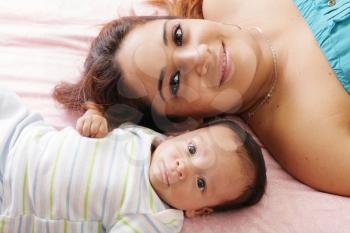 Portrait of happy young attractive hispanic mother lying with her baby on the bed