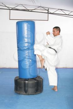 Athletic black belt karate giving a forceful knee kick during a training with a boxing bag 