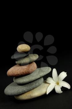 Seven pebbles pyramid in staggered rows, with a white flower, over black