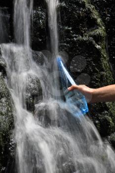 A man's hand fills a bottle of mineral water in waterfalls
