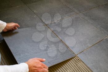 Tiler installing dark ceramic tiles on a floor