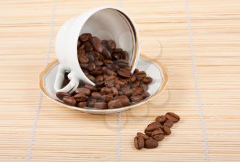 Royalty Free Photo of a Cup and Saucer with Coffee Beans Spilling Out