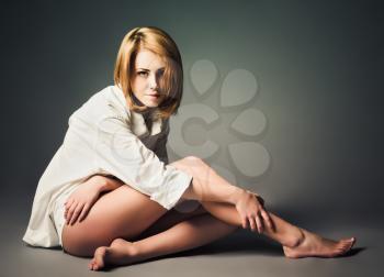 Studio shot: a beautiful young girl in white shirt sits on the floor