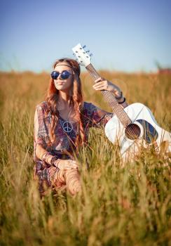 Portrait of a lovely young hippie girl with guitar. Shot in the field