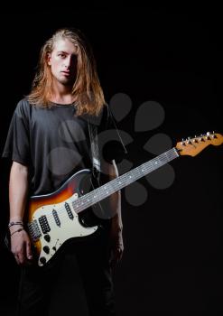 Dramatic studio portrait: a handsome longhaired young man (rock musician) with electric guitar 