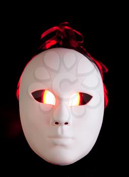 Scary white mask with red eyes on dark background
