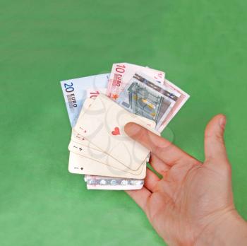 Gambler's hand with four aces on green table and bunch of euros
