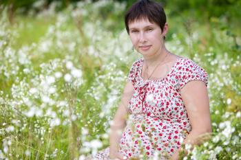 Pregnant woman sitting in chamomile background
