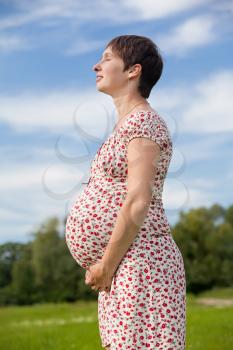 Pregnant woman with closed eyes on green meadow
