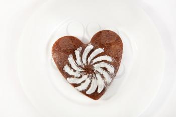 Brown heart shaped cookie with sugar powder on white plate
