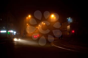 Night scene with moving cars and walking people in the fog
