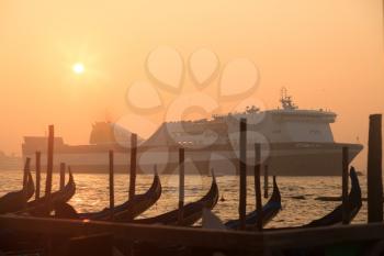 Ferryboat sailing near venetian gondolas at sunrise