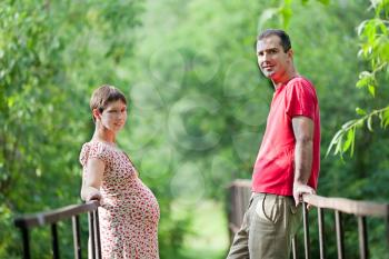 Husband with his pregnant wife on the bridge in green forest
