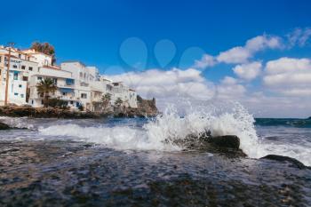 Sea wave with splashes and white houses near seashore at geek island
