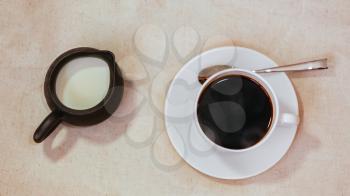 Espresso in white cup and saucer with spoon, milk in jar on grunge vintage background
