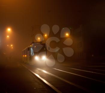 Tram moving on city street in the fog at night
