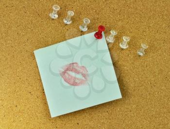 closeup of thumbtacks and kiss note on cork board 