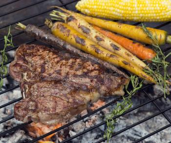 T bone steak cooking on fire with vegetables and herbs
