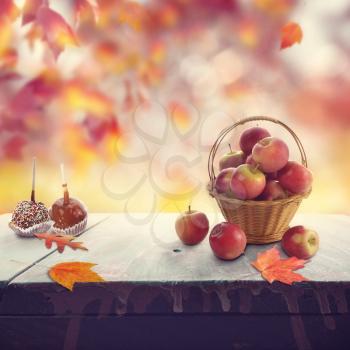 Old wooden table with red apples and autumn leaves