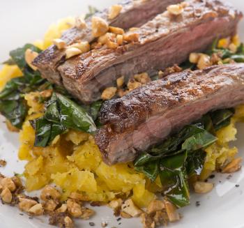 flank steak with mashed plantain , collard greens and ginger peanuts, close up