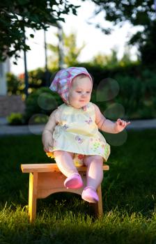 Happy little baby girl sits on a bench at sunset