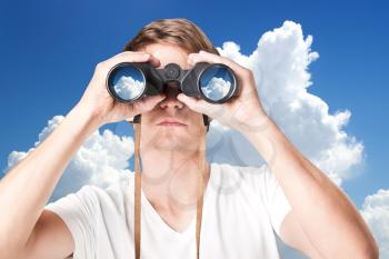 Closeup of handsome young man looking through binoculars against sky 