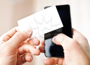Man holding blank business card and dialing numbers on mobile phone 