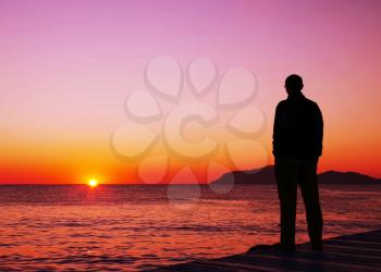 Royalty Free Photo of a Silhouette of a Man Watching a Sunset Over Water