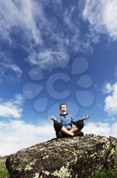Royalty Free Photo of a Man Meditating on a Rock