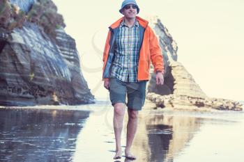 Tourist walking on the beach in the Three Sisters rock formation by New Plymouth coast, New Zealand
