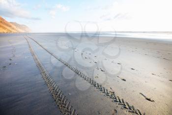 Off road car tyre track on sandy beach, with ocean and blue sky. New Zealand ocean coast