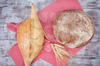 White and brown breads with ears of wheat on wooden background