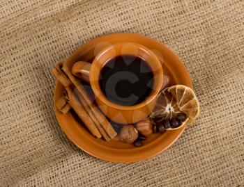 Closeup shot of freshly prepared cup of italian espresso with cinnamon, coffe beans, nuts and lemon over sacking