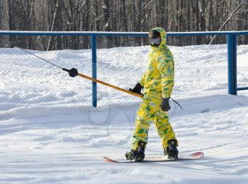 Snowboarder in yellow overalls rises on the lift uphill