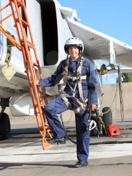 The military pilot in the plane in a helmet in dark blue overalls against the blue sky