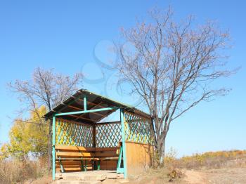 Beautiful wooden arbor in the autumn against the blue sky with a triangular roof