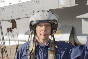 Military pilot in helmet stands near jet plane.
