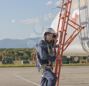 Military pilot in helmet stands near jet plane.