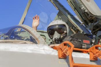 Military pilot in cockpit jet plane with a raised hand.