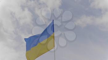 Ukraine flag on the flagpole waving in the wind against a blue sky with clouds. Slow motion.