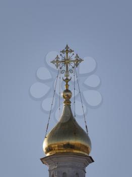 Golden dome with orthodox cross close-up on a blue sky background.