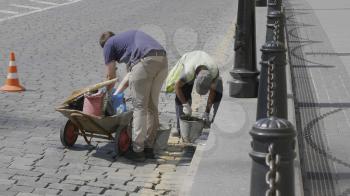 MOSCOW , RUSSIA, June 10, 2019: Two workers loads sand into a wheelbarrow on June 10, 2019 in Moscow, Russia.