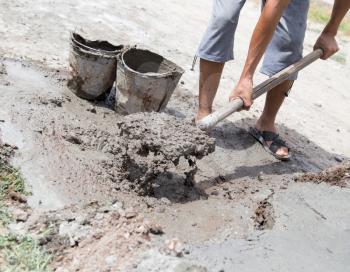 Worker mixes concrete with a shovel at the construction site