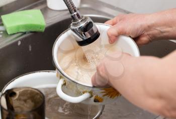 Woman washes spoons under a tap of water .