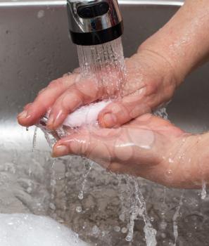 Woman washes her hands with soap under a tap of water .