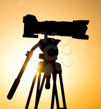 Silhouette of a camera on a tripod at sunset .