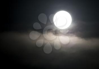 The moon in the haze of the clouds at night .